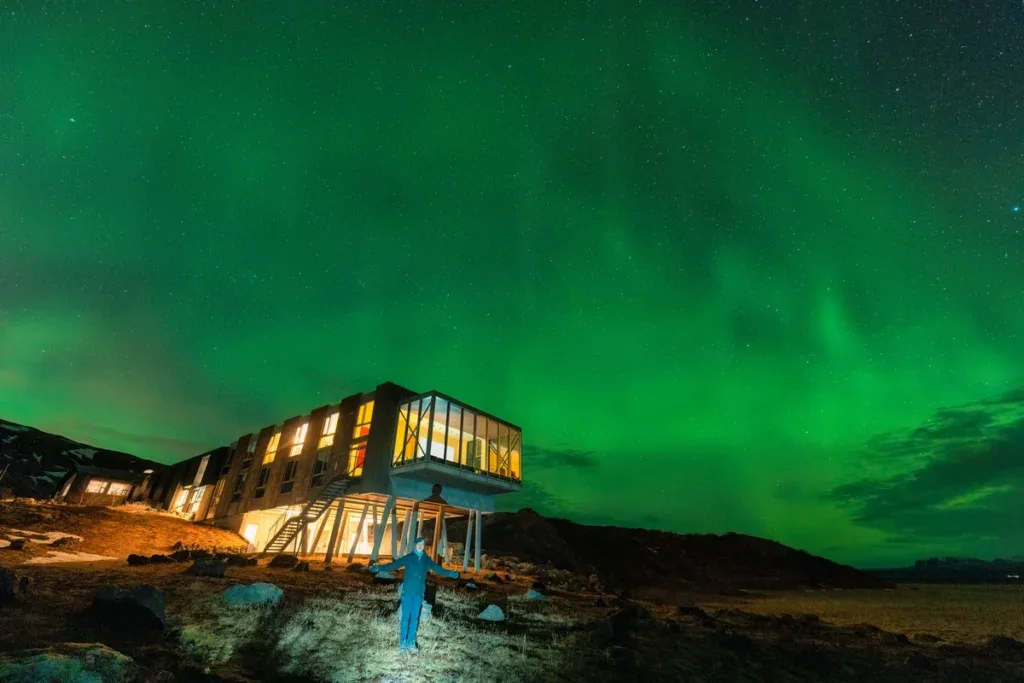 A glass-walled hotel glowing beneath the green aurora borealis on a winter night in Iceland