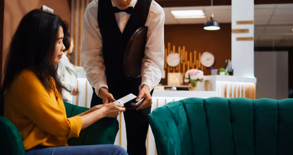 aplikasi keuangan di luar negeri: wanita membayar contactless lewat ponsel pada mesin EDC yang dipegang pelayan kafe