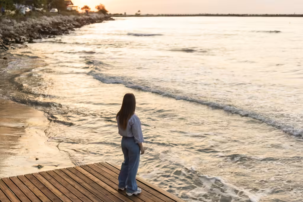viajar y la felicidad: una mujer contempla el mar al atardecer desde un embarcadero