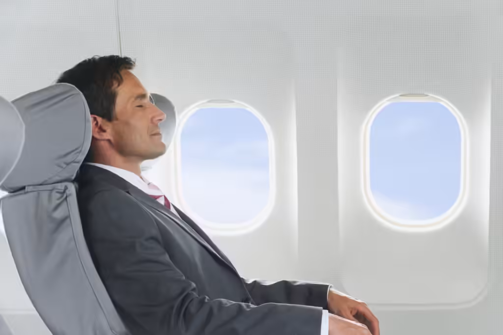 Luxury trip budget: a suited man resting, eyes closed, in a business-class seat beside the aircraft windows