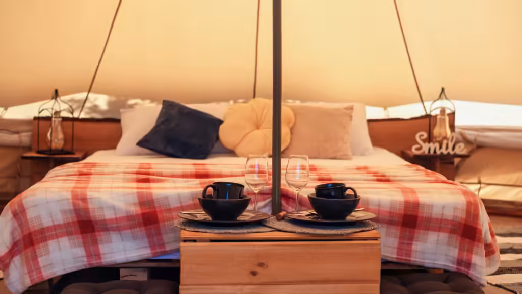 viajes de lujo 2026 para estadounidenses: tienda de glamping con cama doble, manta a cuadros, dos faroles y copas de vino