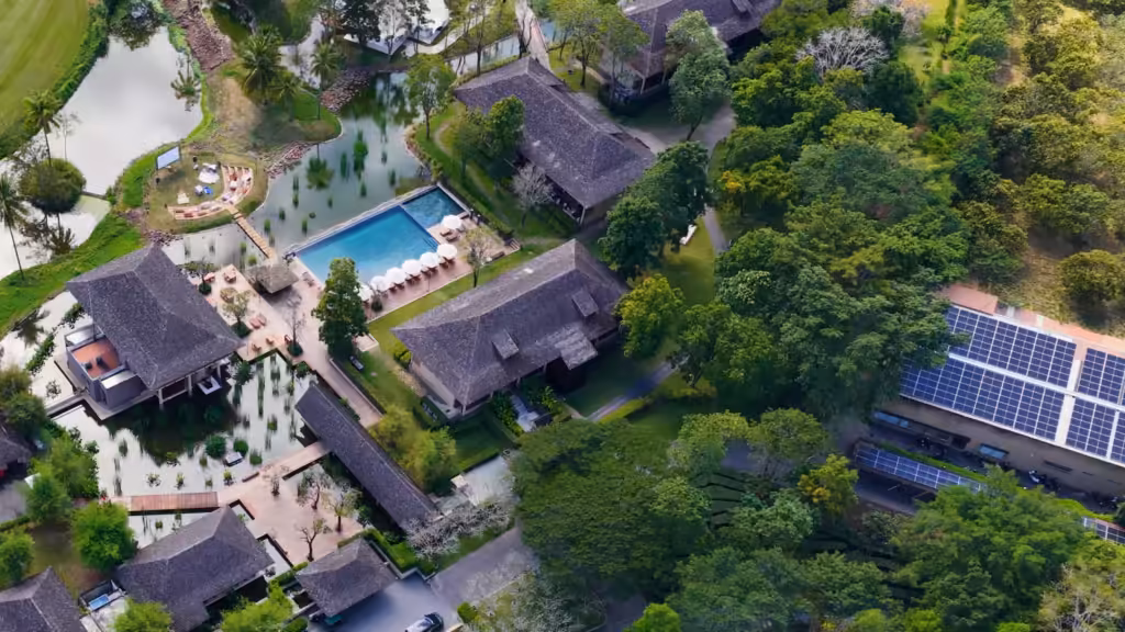 turismo de lujo sostenible: vista aérea de un resort con villas entre árboles, piscina, estanques y paneles solares