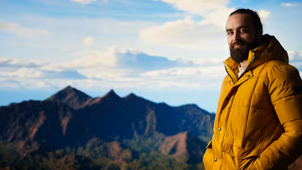 sistem layering iklim berubah-ubah: pria berjanggut dengan jaket down kuning berdiri di puncak gunung saat matahari terbit