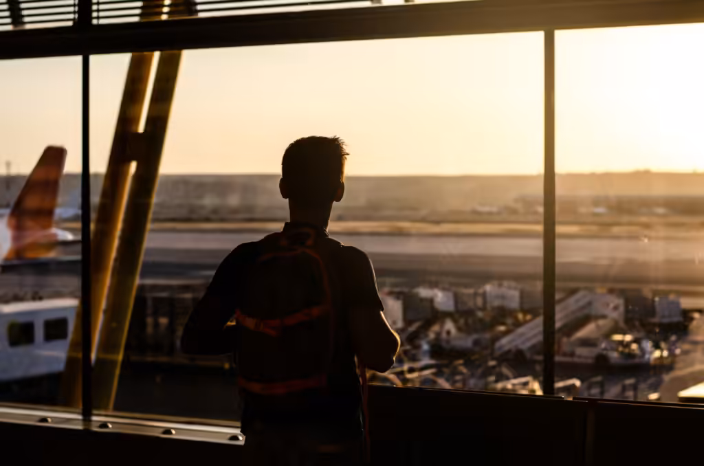 Fadiga do retorno ao normal: viajante em pé diante da janela do terminal, ao pôr do sol