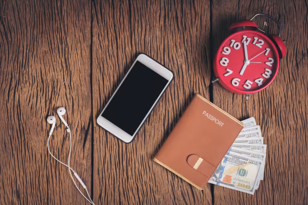 Barang bawaan penting saat traveling: paspor, uang tunai, ponsel, earphone, dan jam weker tertata di meja